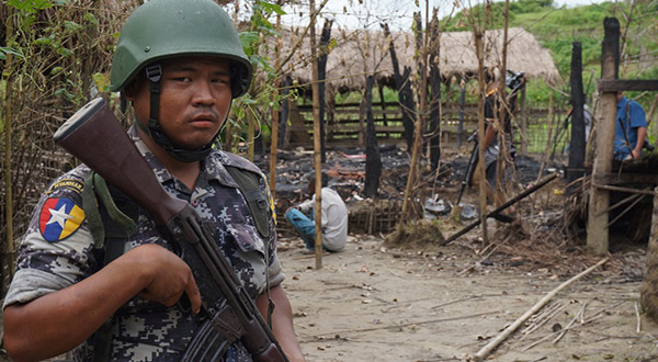 A Myanmar border guard police officer stands guard in front of the remains of a house
